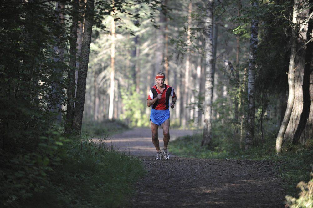 Yksinäinen lenkkeilijä juoksemassa metsäpolulla.