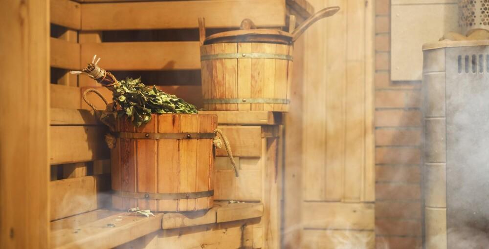 Kuvituskuva. Lämmin sauna. Kiukaasta nousee hyöryä ja saunan lauteilla on saunavihta ja vettä täynnä oleva saunakiulu.
