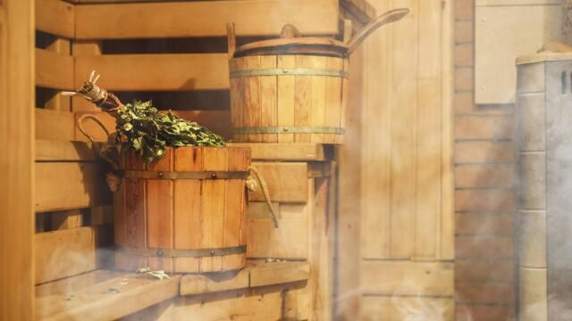 Kuvituskuva. Lämmin sauna. Kiukaasta nousee hyöryä ja saunan lauteilla on saunavihta ja vettä täynnä oleva saunakiulu.