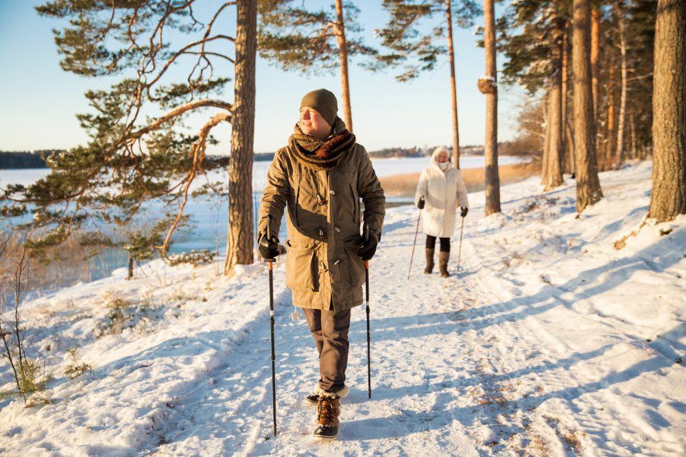 Kaksi henkilöä sauvakävelylenkillä. Kuvan henkilöt kävelevät pitkin lumista metsäpolkua keskellä talvea.