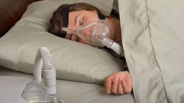 Kuvituskuva. Nainen nukkuu CPAP-laitteen nenä-suumaski kasvoillaan.