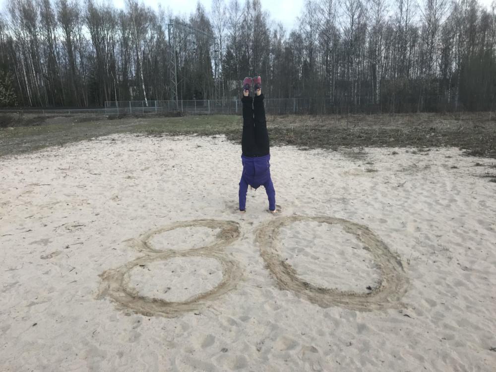 Hengitysliiton liikunnan asiantuntija Veera Farin seisoo käsillään hiekkakentällä. Hiekkaan on piirretty iso 80.