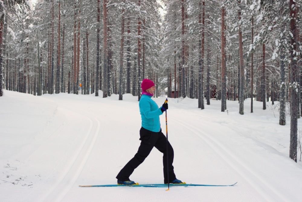 Nainen suksilla toinen jalka eteenpäin ojennettuna ja polvet koukistettuina. 