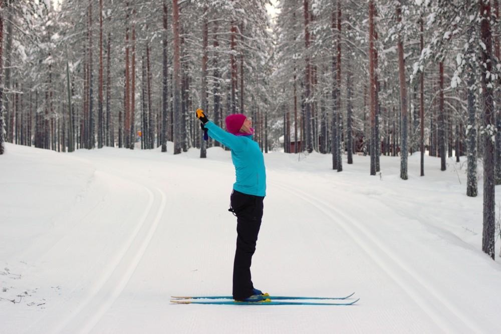 Naisen suksilla. Hänellä on molemmista sauvoista leveä ote ja hän on vienyt sauvat taakse päänsä päälle. 