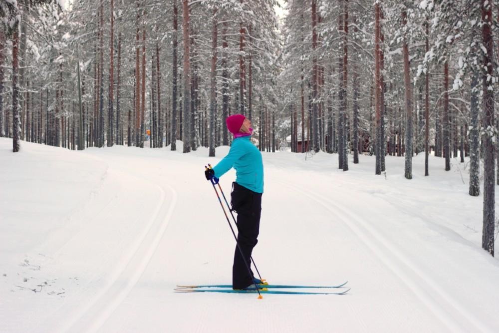 Nainen suksilla avaa rintakehäänsä ja katsoo yläviistoon. Hänen kätensä on viety taakse.