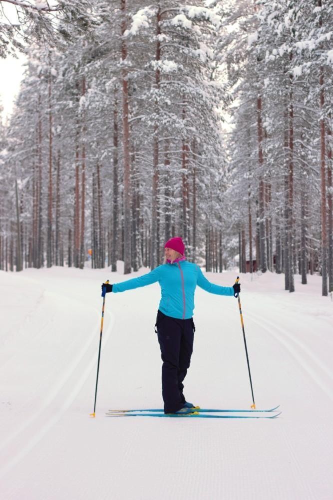 Nainen suksilla kiertää vartaloaan sivulle sauvat käsissään siten, että toinen sauva on suksien takana. 