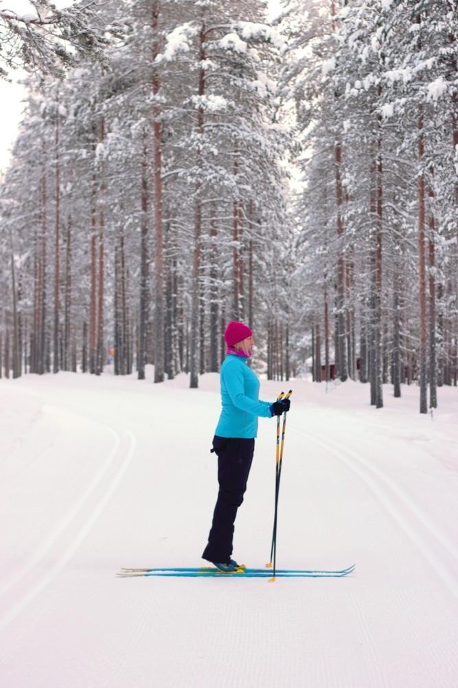 Nainen  suksilla on noussut varpailleen  ja pitää sauvoja edessään. 