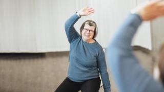 Nainen venyttelee kylkeään tuolilla istuessaan.