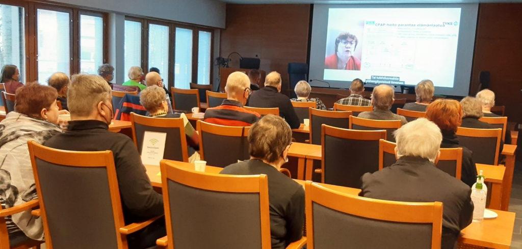 Luentosalissa katsotaan valkokankaalta luentotallennetta.